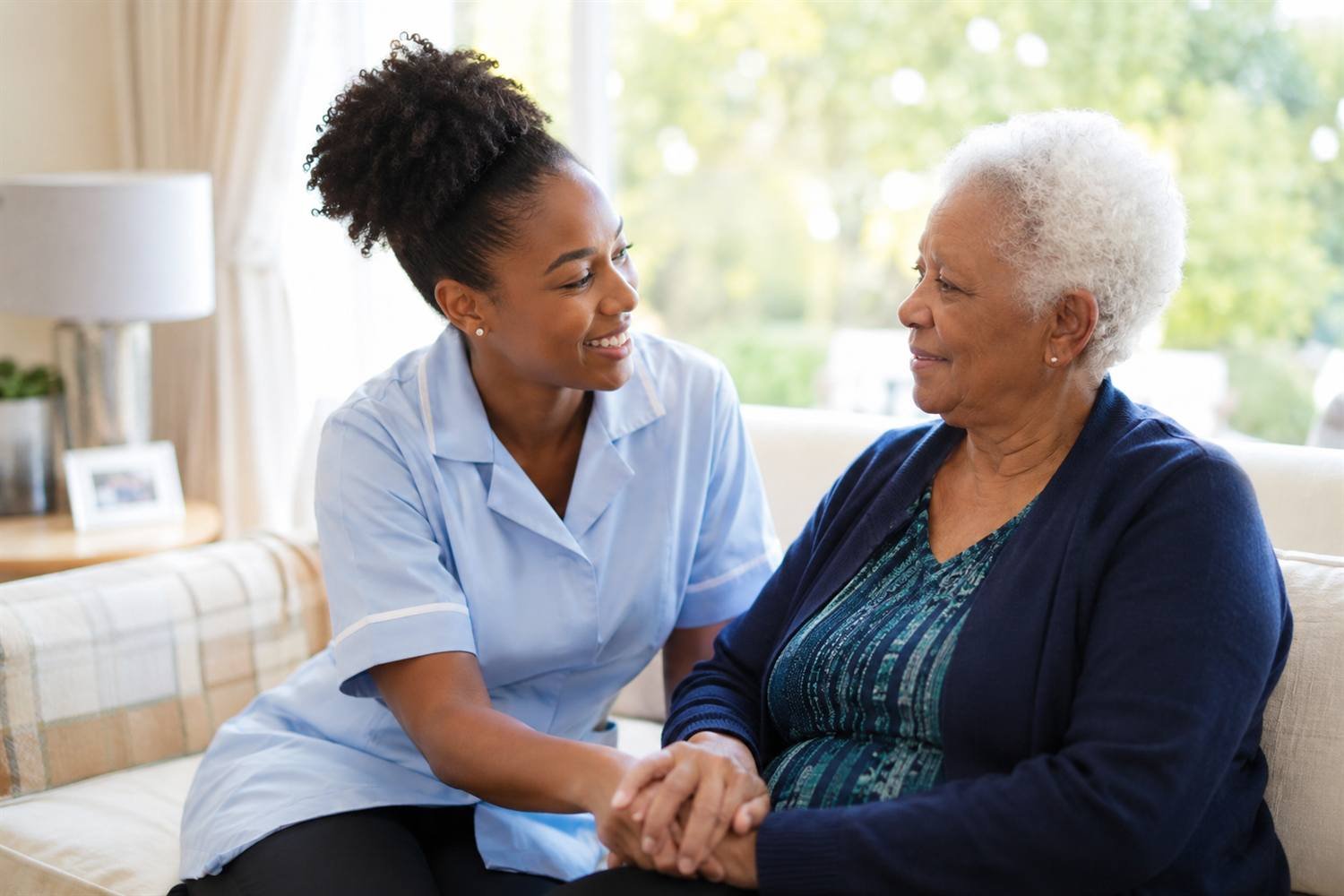 A Bockarie caregiver sitting beside a client in her living room, holding her hands as they talk.